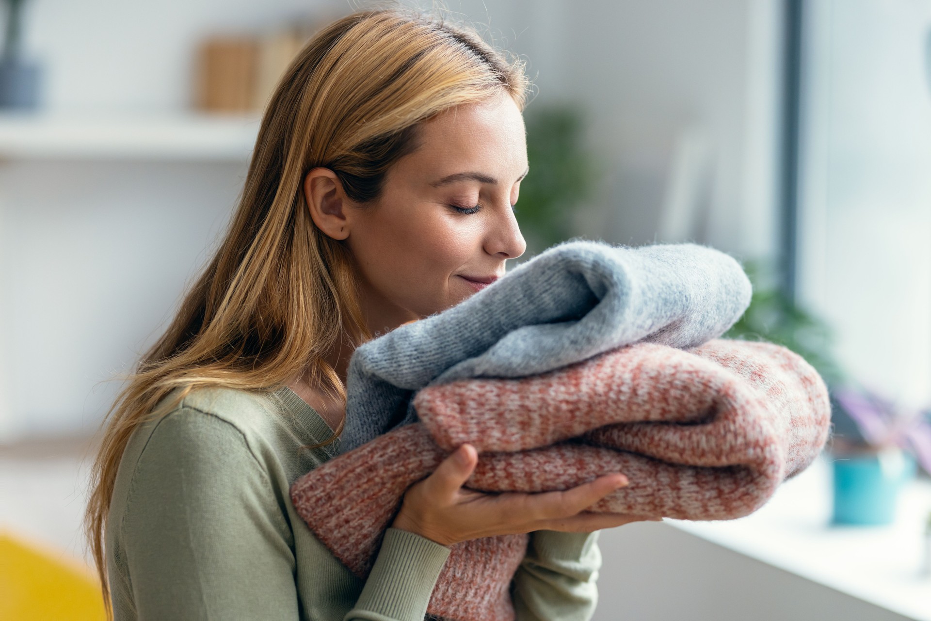 Belle jeune femme tenant et sentant des vêtements propres à la maison.